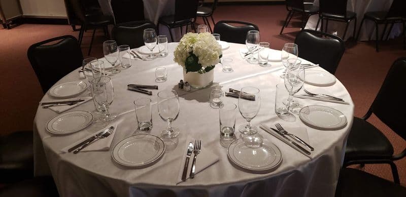 Round table set with white linen, glassware, and a hydrangea centerpiece